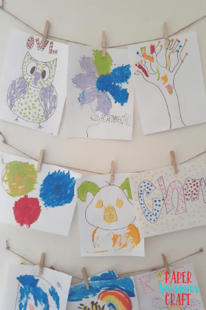Collection of toddler Q-tip paintings hanging on a wall with clothespins.