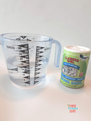 Measuring cup and baking soda on a white counter.