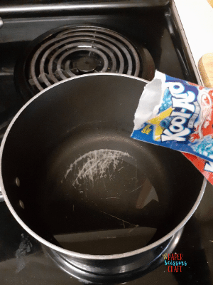 Kool-Aid packet being poured into a pot on a stove that has water in it.