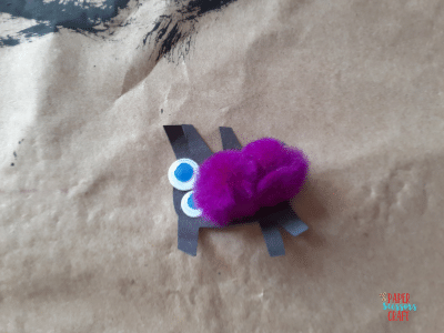 Black construction paper spider with googly eyes and purple pom poms.