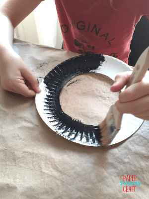 Paper plate with inner circle cut out being painted black.