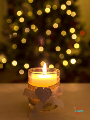 White candle lit and in front of a Christmas tree.