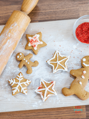 Gingerbread cookies on a table with red sprinkles and a rolling pin.