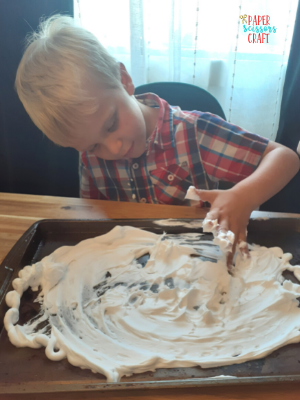 Child playing with shaving cream on cookie sheet.