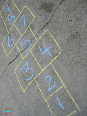 Hopscotch written in blue and yellow chalk on a driveway.
