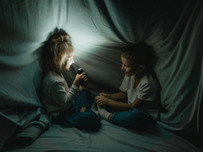 Kids in a sheet fort with a flashlight lit up.