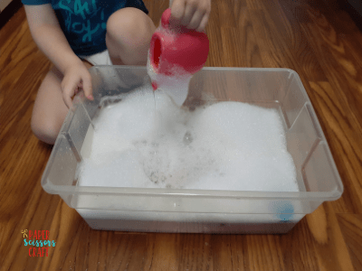 Child demonstrating water play with soapy water in a plastic container.