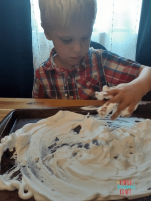 Little boy playing by putting hands in shaving cream on a baking sheet.