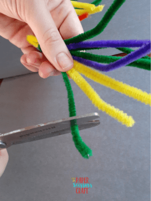 Pipe cleaners twisted together and being cut with scissors.
