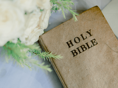 The Holy Bible placed on a counter next to a white flower arrangement.