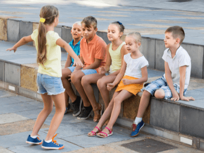 Kids outside sitting on a stone bench and playing charades.