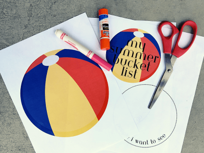 Paper, pink marker, glue stick, and scissors on a counter demonstrating what the Summer bucket list craft looks like.